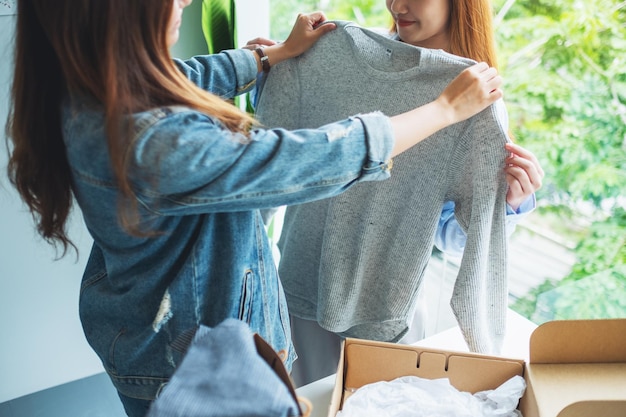 Twee jonge vrouwen die een postpakketdoos ontvangen en thuis kleding passen voor bezorging en online winkelconcept