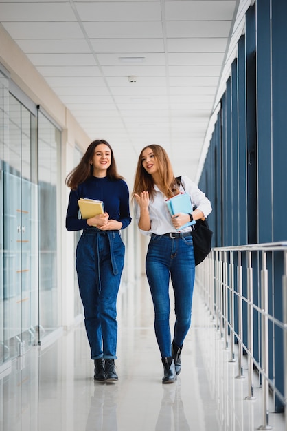 Twee jonge vrouwen die met boek chatten terwijl ze in universiteitsgang staan