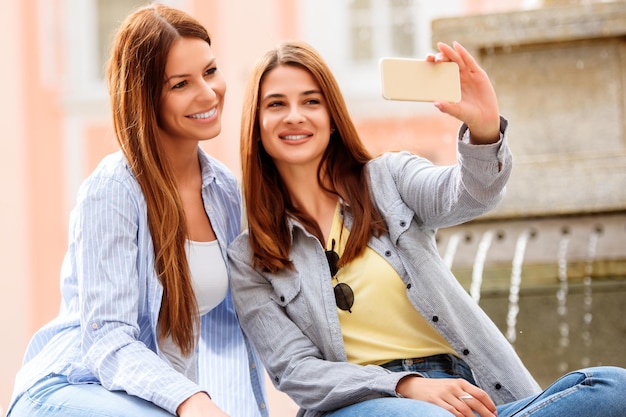 Twee jonge vrouwen die op straat een smartphone gebruiken om selfies te maken