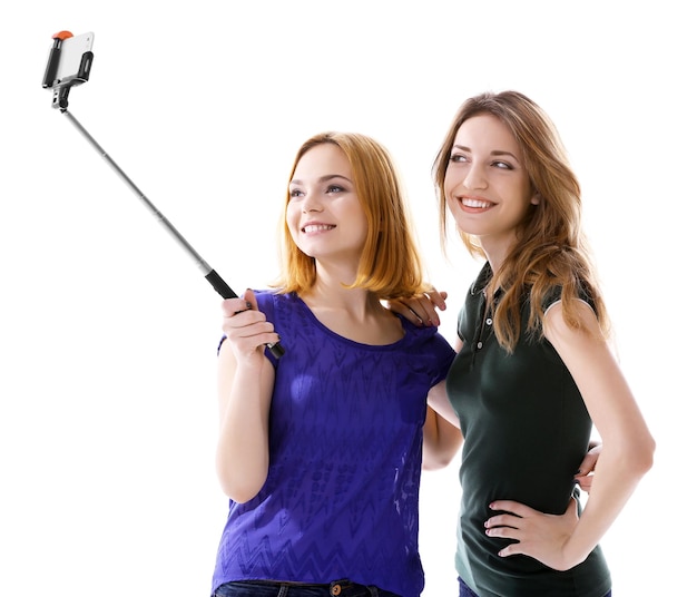 Foto twee jonge vrouwen die selfie met mobiele telefoon nemen die op wit wordt geïsoleerd