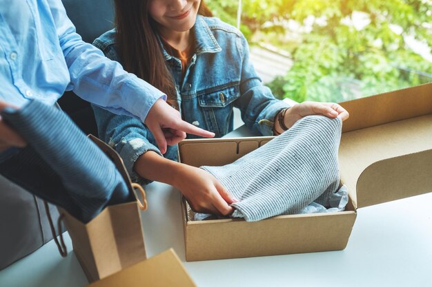 Twee jonge vrouwen die thuis een postpakketdoos met kleding ontvangen en openen voor bezorging en online winkelconcept