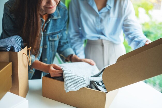 Twee jonge vrouwen die thuis een postpakketdoos met kleding ontvangen en openen voor bezorging en online winkelconcept
