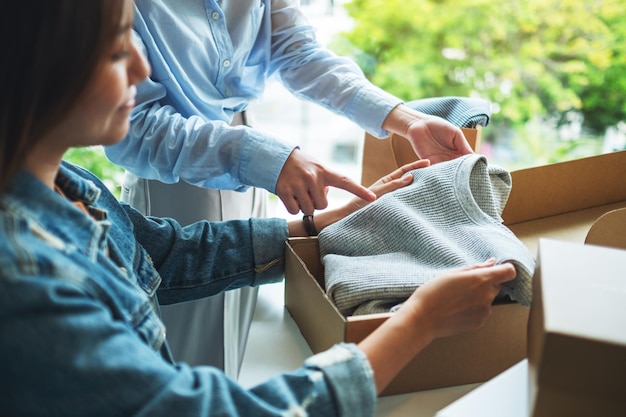 Twee jonge vrouwen die thuis een postpakketdoos met kleding ontvangen en openen voor bezorging en online winkelconcept