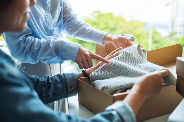 Twee jonge vrouwen die thuis een postpakketdoos met kleding ontvangen en openen voor bezorging en online winkelconcept