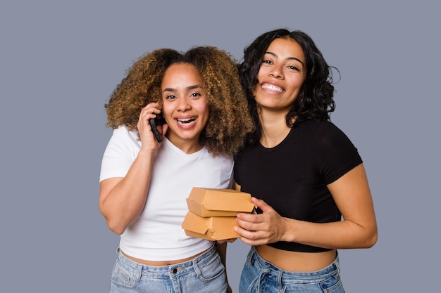 Twee jonge vrouwen, een Latina en een met Afro-haar, lachen terwijl ze pizza's en hamburgers vasthouden