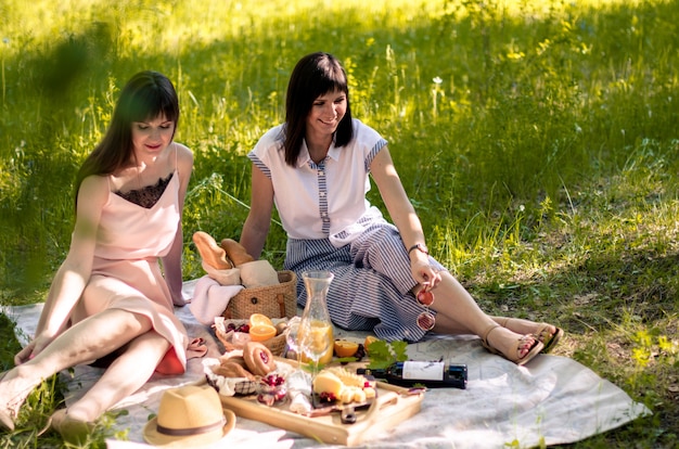 Twee jonge vrouwen in park buiten op zonnige dag. Picknick op het gras met pizza, brood, sinaasappelsap, kaas en fruit