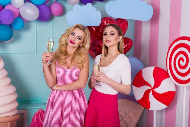 Twee jonge vrouwen in roze jurken houden glazen champagne.