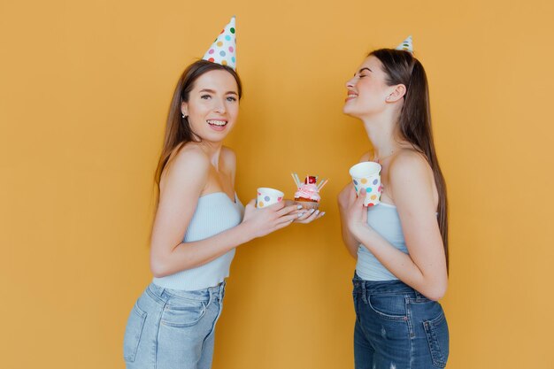 Twee jonge vrouwen in verjaardagshoeden die verjaardag vieren