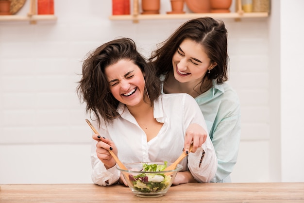 Twee jonge vrouwen koken en knuffelen in de keuken