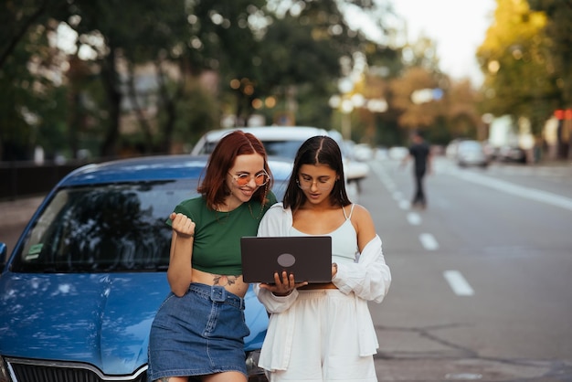 Twee jonge vrouwen met een laptop bij de auto