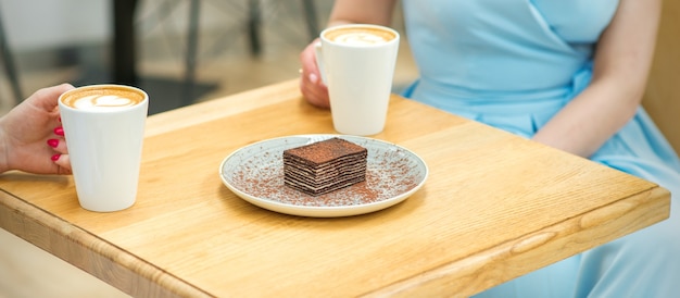 Twee jonge vrouwen met kopjes koffie en stukjes cake zitten aan tafel in een café buitenshuis