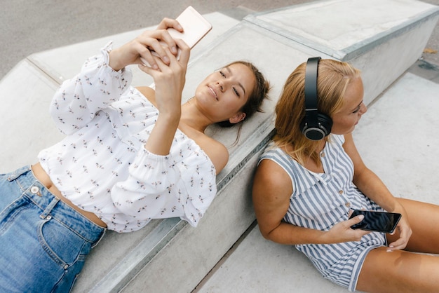 Twee jonge vrouwen met mobiele telefoons en koptelefoons in een skatepark