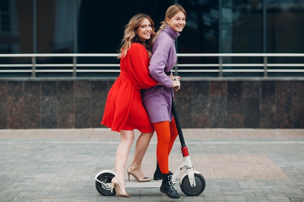 Twee jonge vrouwen rijden op elektrische scooter in de stad