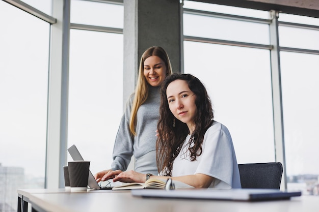 Twee jonge vrouwen werken in een modern kantoor Werk kantoorruimte met grote ramen Vrouw manager werkt aan het bureau zit in het kantoor