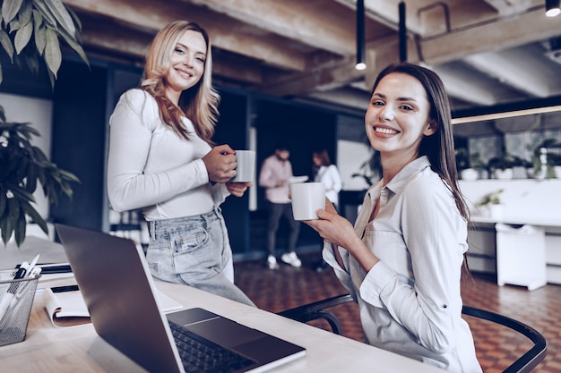 Twee jonge vrouwencollega's die koffie in bureau drinken