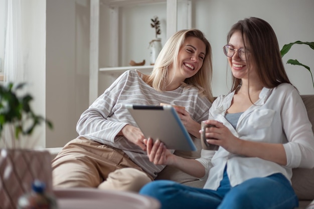 Twee jonge vrouwenvrienden die tablet gebruiken die samen glimlachend en pret op de bank zit