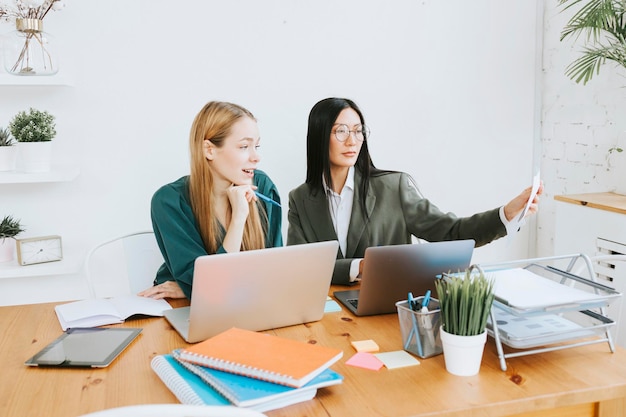 Twee jonge zakelijke vrouwelijke professionals in formele kleding werken in een modern kantoor met behulp van laptop tablet brainstorm en zoeken naar oplossingen samen zelfverzekerd onafhankelijk Aziatisch meisje lost problemen op