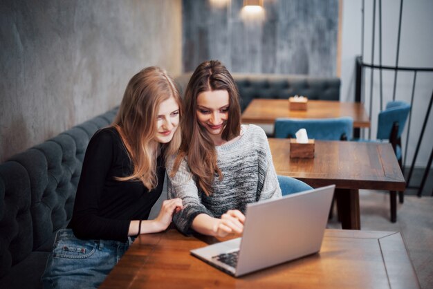 Twee jonge zakelijke vrouwen zitten aan tafel in café. Meisje toont collega-informatie op laptop scherm. Vrienden ontmoeten, samen eten. Freelancers aan het werk.