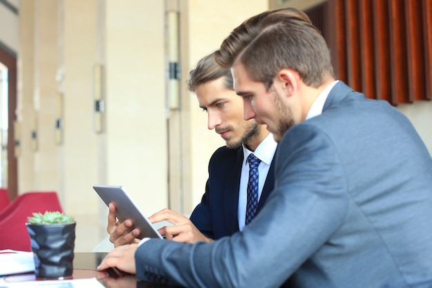 Twee jonge zakenlieden die touchpad gebruiken tijdens vergadering.
