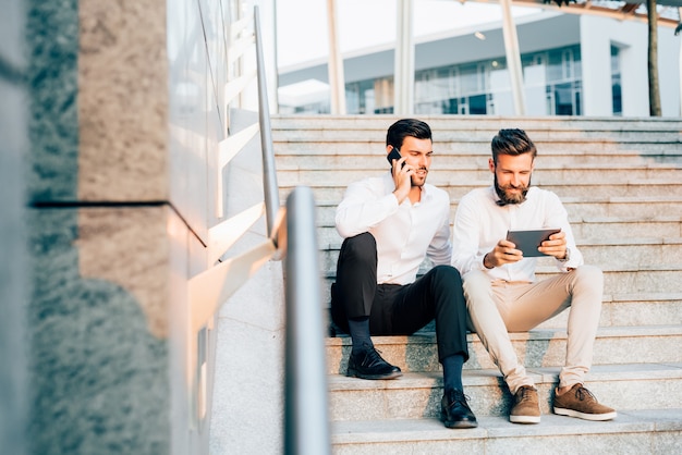 Twee jonge zakenman met behulp van technologische apparaten