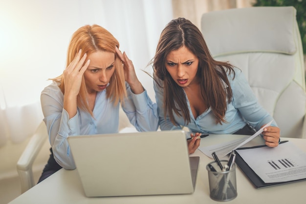 Twee jonge zakenvrouwen kijken op een laptop op kantoor met een zorgelijke uitdrukking op hun gezicht.