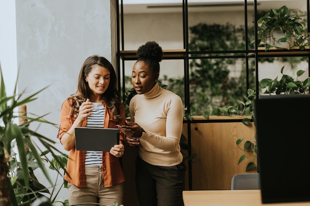 Foto twee jonge zakenvrouwen met een digitale tablet staan in het moderne kantoor