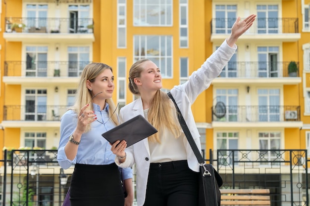 Twee jonge zakenvrouwen op straat praten en kijken in het scherm van digitale tablet