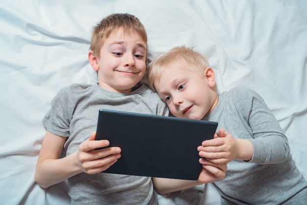 Twee jongens die in bed liggen en op iets op een tablet letten. Gadget Vrije tijd