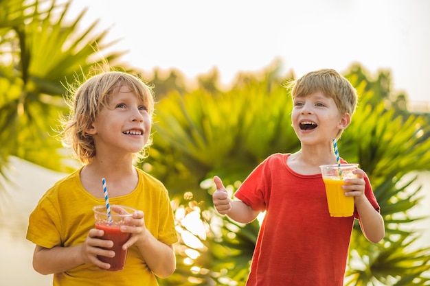 Twee jongens drinken gezonde smoothies tegen de achtergrond van palmbomen Mango- en watermeloensmoothies Gezonde voeding en vitamines voor kinderen