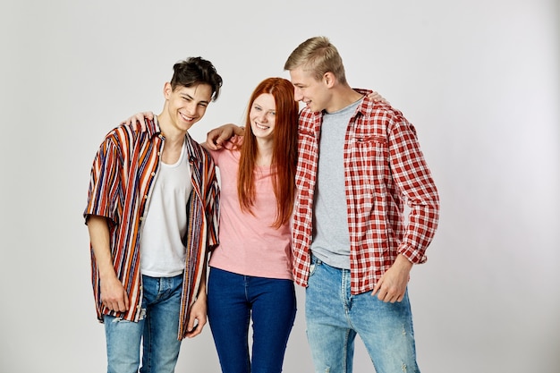 Twee jongens en een meisje in heldere kleurrijke kleding lachen op de witte achtergrond in de studio