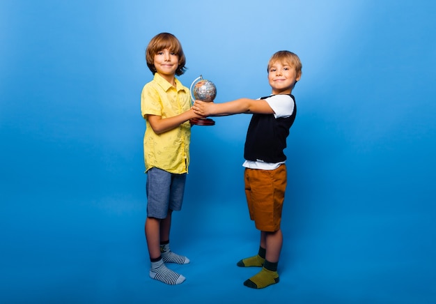 Twee jongens houden een wereldbol op een blauwe achtergrond. onderwijsconcept. kopieer ruimte