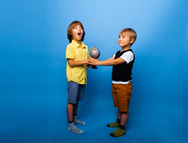 Twee jongens houden een wereldbol op een blauwe achtergrond. onderwijsconcept. kopieer ruimte