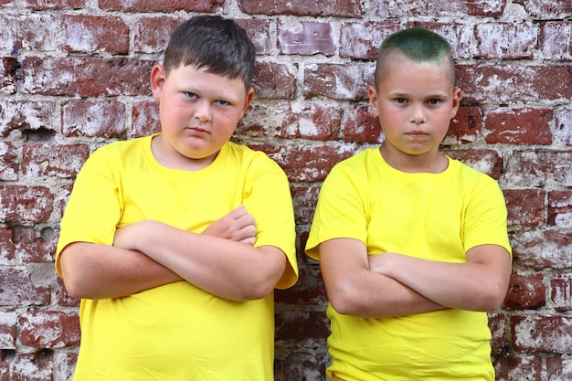 Twee jongens in gele T-shirts staan met hun armen over elkaar voor een bakstenen muur. Hoge kwaliteit foto