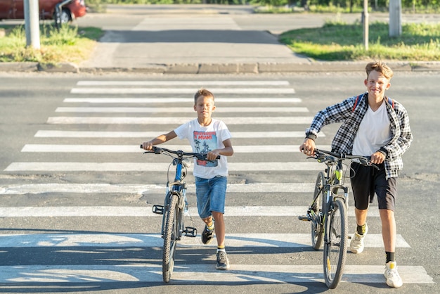 Twee jongens lopen en fietsen door een voetgangerskruis en houden zich aan de regels voor het oversteken als fietsers