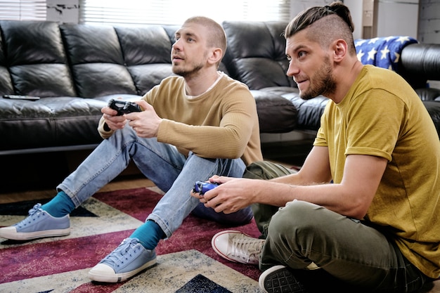 Twee jongens met joysticks die videogames spelen op de vloer in de woonkamer van het appartement dat ze delen