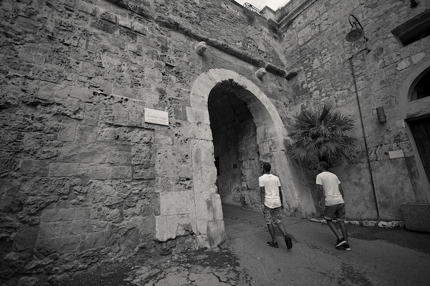 Twee jongens van achteren staan op het punt een oude deur binnen te gaan die behoort tot het historische centrum van Cagliari