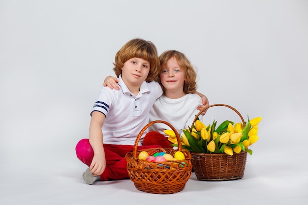 Foto twee jongetjes zitten met een mand met paaseieren en een mand met tulpen. witte achtergrond. grappige momenten