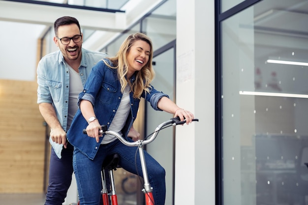 Twee kantoormedewerkers lachen samen op een tandemfiets.