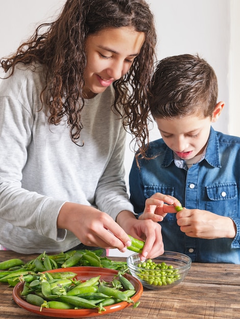 Twee kinderen die verse erwten uit hun peulen halen