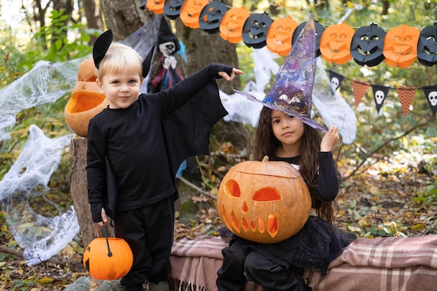 twee kinderen meisje en jongen in halloween kostuum met pompoenen in halloween decoraties buiten