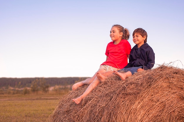 Twee kinderen zitten bij zonsondergang op een hooiberg in het veld