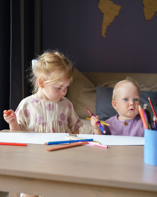 Twee kinderen zus en baby jongen broer tekenen met potloden samen thuis