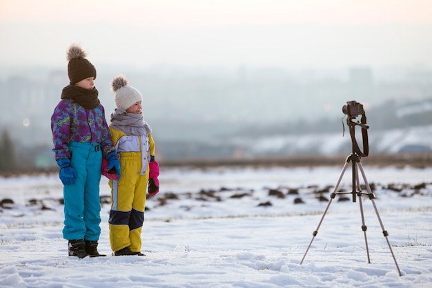 Twee kinderenjongen en meisje die pret buiten in de winter spelen met fotocamera op een driepoot op sneeuw behandeld gebied.