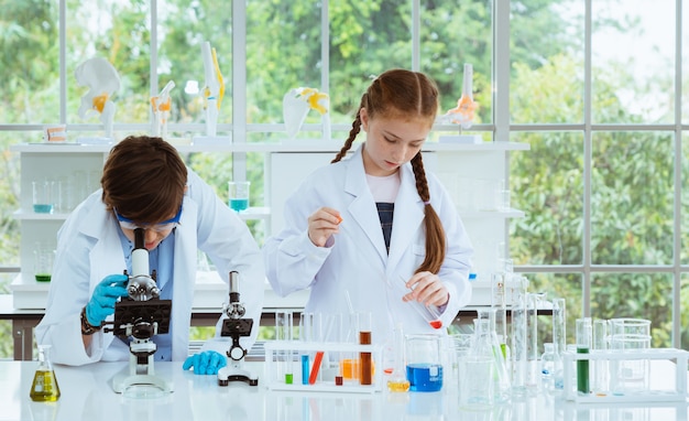 Twee kinderenwetenschappers die experimenten chemisch maken met een microscoop in de laboratoriumkamer.