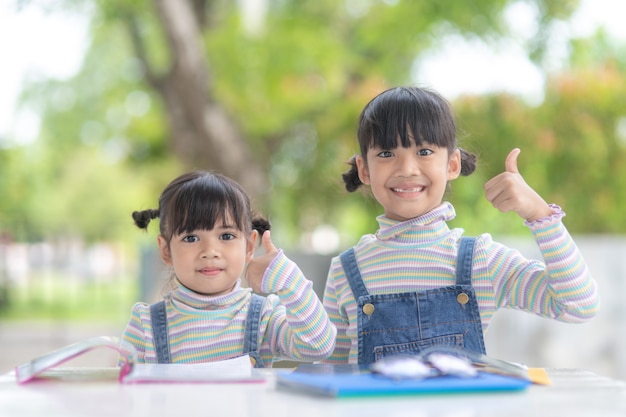 Twee kleine Aziatische studentenmeisjes die het boek op tafel lezen