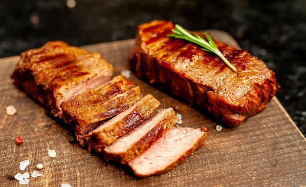 twee kleine gegrilde biefstuk op een snijplank met kruiden op een achtergrond van zwarte steen