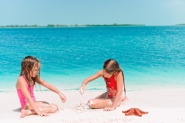 Twee kleine gelukkige meisjes hebben veel plezier op tropisch strand samen spelen