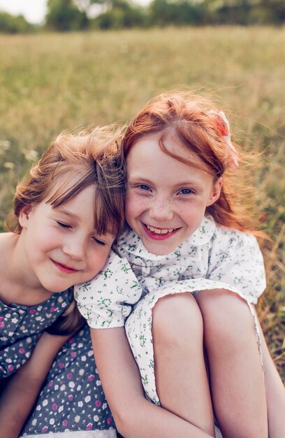 Foto twee kleine gelukkige meisjes in lichte zomerjurken zitten in een veld op het gras. gelukkige jeugd.