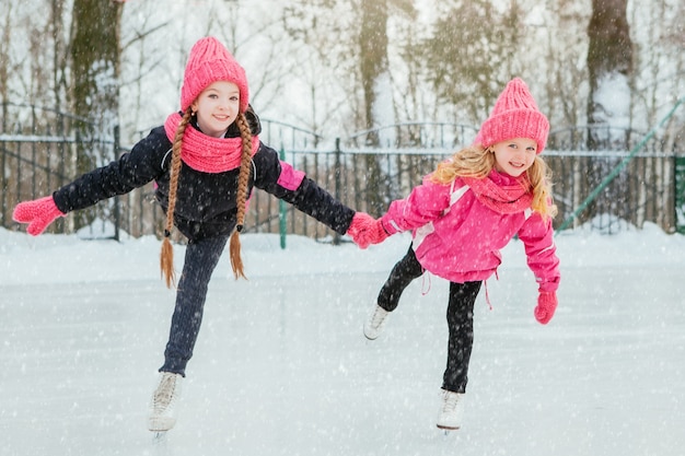 Twee kleine glimlachende meisjes schaatsen op ijs in roze slijtage en handgemaakte sjaals.