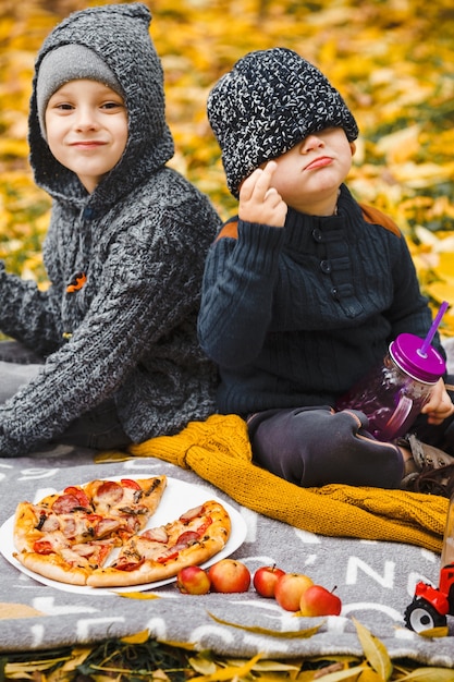 Twee kleine jongens broers zitten op plaid in park en drinken eten zelfgemaakte pizza rode appels